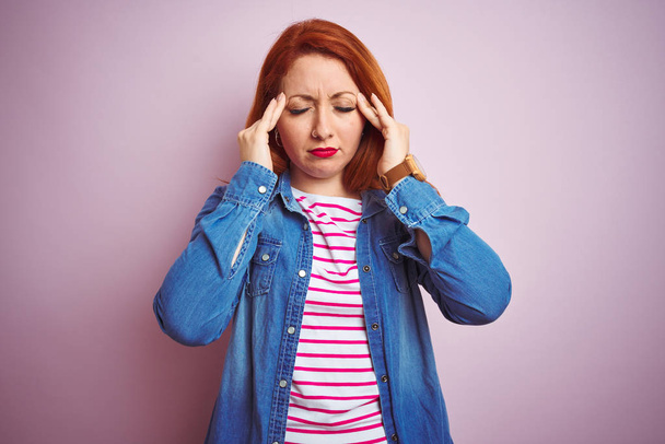 Krásná zrzka žena v džínové košili a pruhované tričko přes izolované růžové pozadí s rukou na bolesti hlavy, protože stres. Trpící migréna. - Fotografie, Obrázek