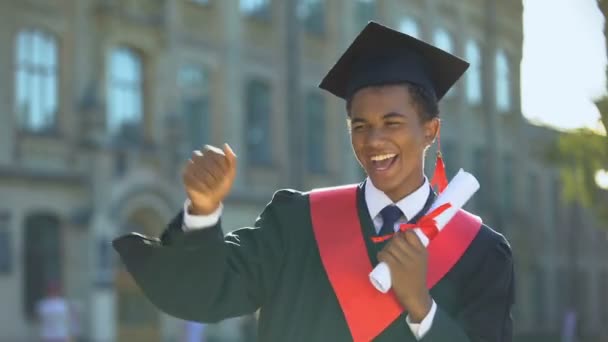 Alegre baile masculino celebrando la graduación al aire libre universidad, conocimiento - Imágenes, Vídeo