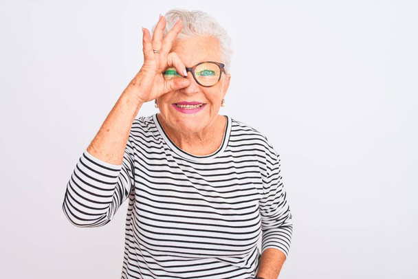 Senior grey-haired woman wearing striped navy t-shirt glasses over isolated white background doing ok gesture with hand smiling, eye looking through fingers with happy face. - Fotografie, Obrázek