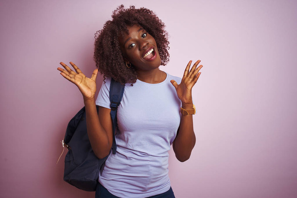 Jeune femme afro-touristique africaine portant un sac à dos debout sur fond rose isolé célébrant fou et étonné pour le succès avec les bras levés et les yeux ouverts hurlant excités. Concept gagnant
 - Photo, image