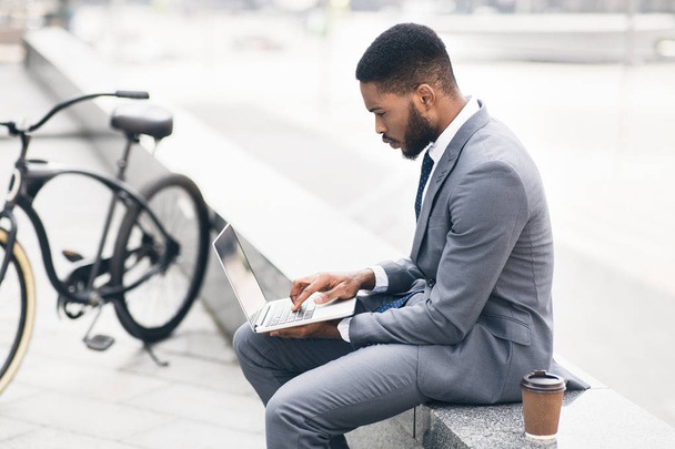 Серьезный бизнесмен использует ноутбук на открытом воздухе с велосипедом поблизости
 - Фото, изображение
