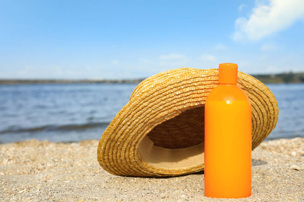 Bottle of sun protection body cream and hat on beach, space for design - Foto, immagini