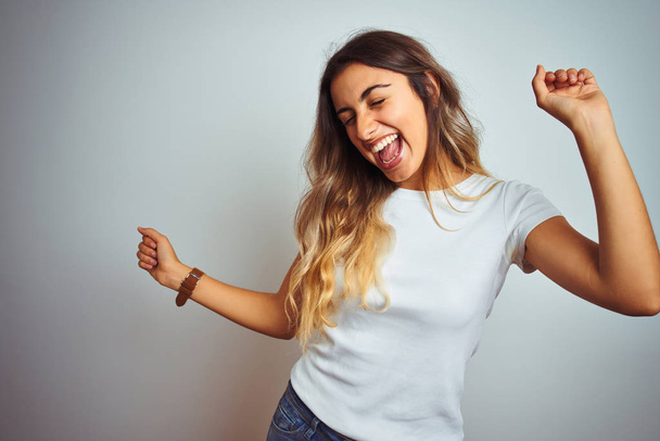 Young beautiful woman wearing casual white t-shirt over isolated background Dancing happy and cheerful, smiling moving casual and confident listening to music - Photo, Image