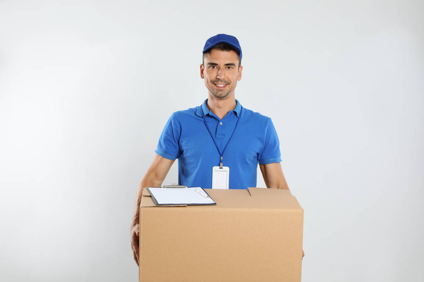 Happy young courier with cardboard box and clipboard on white background - Foto, Imagen