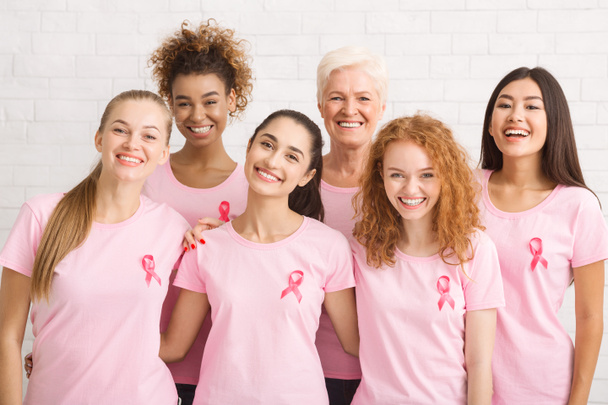 Damen in rosafarbenen Schleifen-T-Shirts posieren drinnen auf weißem Hintergrund - Foto, Bild