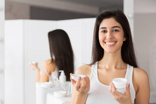 Young Woman Holding Face Cream Product Standing In Bathroom - Photo, image