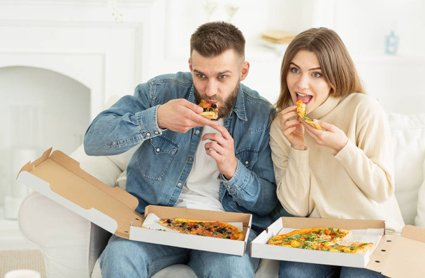 Νεαρό ζευγάρι απολαμβάνει τρώει πίτσα και βλέποντας τηλεόραση στο σπίτι - Φωτογραφία, εικόνα