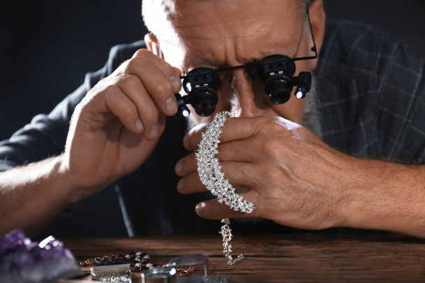 Male jeweler evaluating diamond necklace in workshop - Foto, imagen