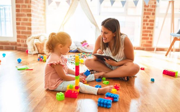 Красивый психолог и блондинка девочка делает терапию здания башни с использованием пластиковых блоков в детском саду
 - Фото, изображение
