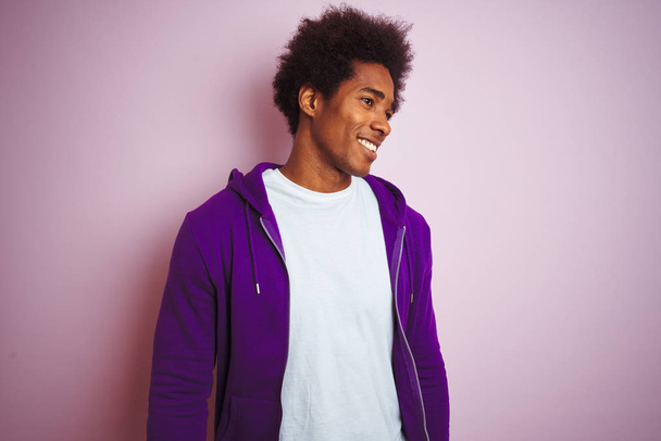 Jovem afro-americano vestindo camisola roxa em pé sobre fundo rosa isolado olhando para o lado com sorriso no rosto, expressão natural. Rindo confiante
. - Foto, Imagem