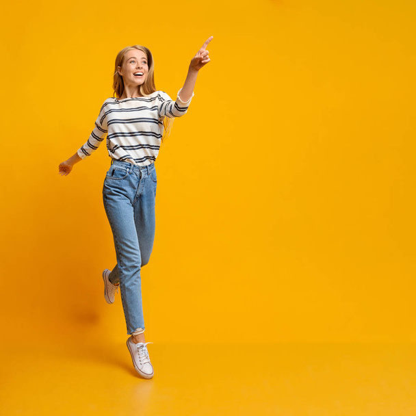 Chica alegre saltando y señalando en el espacio de copia en el fondo amarillo
 - Foto, Imagen