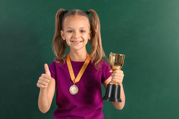 Happy girl with golden winning cup and medal near chalkboard - Zdjęcie, obraz