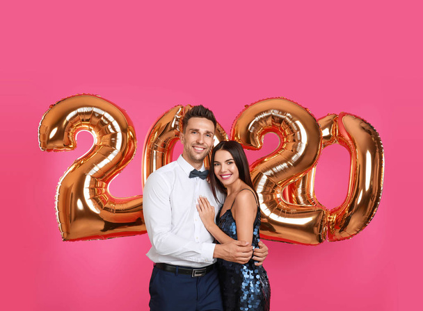 Feliz pareja joven cerca de globos dorados 2020 sobre fondo rosa. Celebración de Año Nuevo
 - Foto, imagen