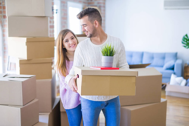 Молодая красивая влюбленная пара переезжает в новый дом, держа картонные коробки очень счастливой и веселой для новой квартиры
 - Фото, изображение