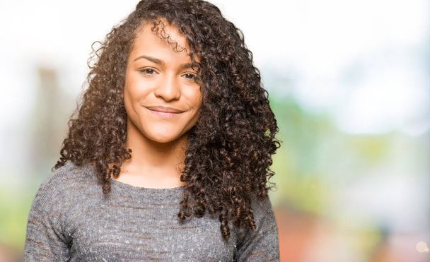 Young beautiful woman with curly hair wearing grey sweater Hands together and fingers crossed smiling relaxed and cheerful. Success and optimistic - Photo, Image