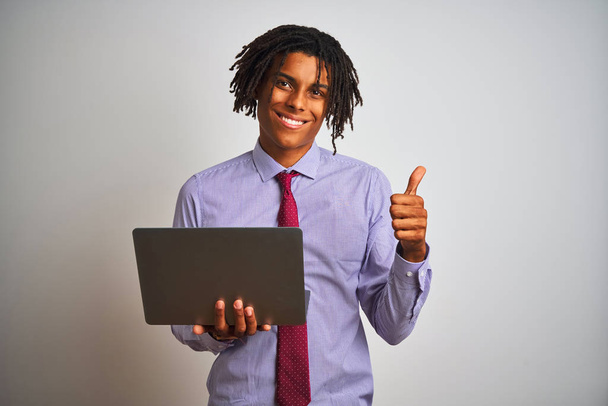 Afro american businessman with dreadlocks using laptop over isolated white background happy with big smile doing ok sign, thumb up with fingers, excellent sign - Foto, imagen
