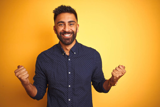 Young handsome indian businessman wearing shirt over isolated yellow background celebrating surprised and amazed for success with arms raised and open eyes. Winner concept. - Photo, Image