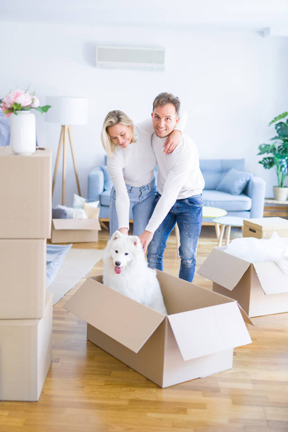Young beautiful couple with dog hugging at new home around cardboard boxes - Fotografie, Obrázek