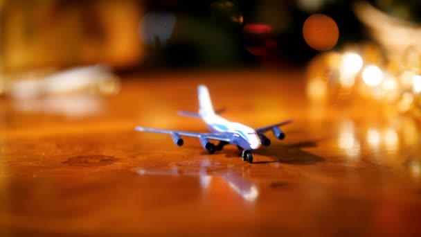 Closeup felvételeit kis játék repülőgép fából készült asztal ellen izzó színes karácsonyi fények. Az utazás és a turizmus fogalma a téli szünnapokon és ünnepségeken. - Felvétel, videó