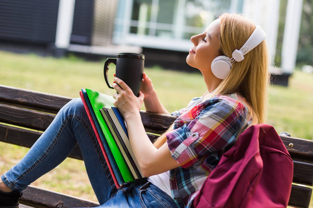 Female student with headphones enjoys listening music and drinking coffee outdoor. - Photo, image