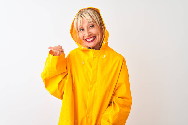 Middle age woman wearing rain coat with hood standing over isolated white background smiling with happy face looking and pointing to the side with thumb up. - Φωτογραφία, εικόνα