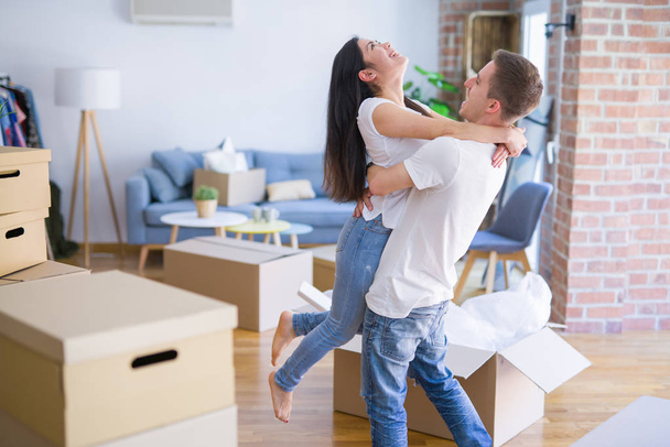 Young beautiful couple hugging at new home around cardboard boxes - Foto, imagen