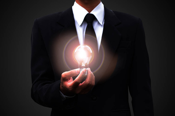 Бізнесмен чорний костюм, що тримає підсвічену лампочку, концепція аналізу стратегії
. - Фото, зображення