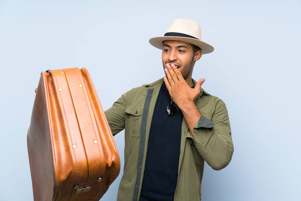 Joven hombre guapo sosteniendo un maletín vintage sobre fondo azul aislado con sorpresa y expresión facial conmocionada
 - Foto, imagen