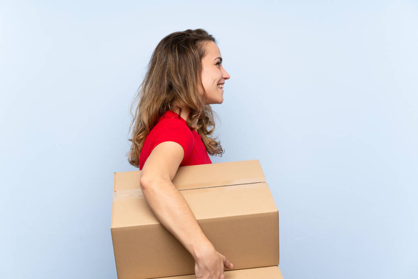 Mujer rubia joven sosteniendo una caja para moverla a otro sitio en posición lateral
 - Foto, Imagen