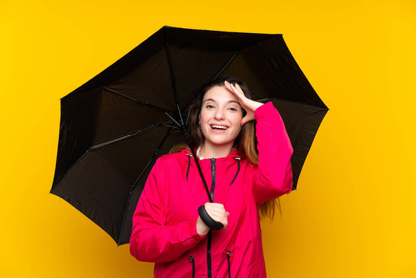 Sarı arka planda şemsiyesini tutan esmer kız şaşırmış ve şok olmuş bir yüz ifadesi var. - Fotoğraf, Görsel