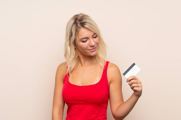 Jovem loira sobre fundo isolado segurando um cartão de crédito
 - Foto, Imagem