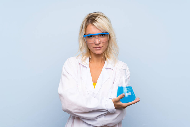 Young blonde woman over isolated background with a scientific test tube - Valokuva, kuva