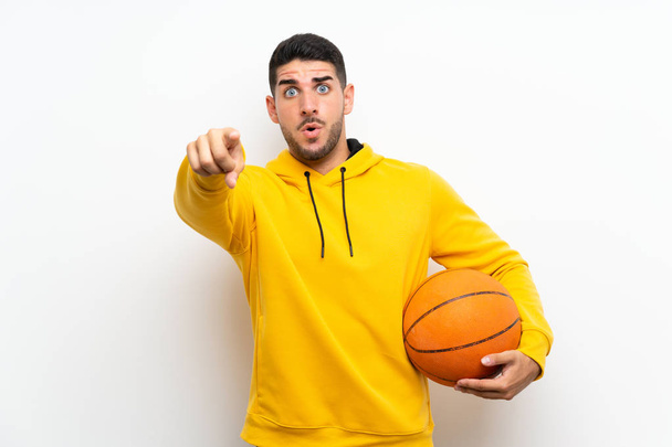 Bello giovane giocatore di basket uomo oltre isolato muro bianco sorpreso e che punta davanti
 - Foto, immagini