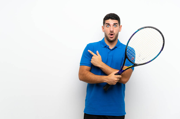 Handsome young tennis player man over isolated white wall surprised and pointing side - Photo, Image