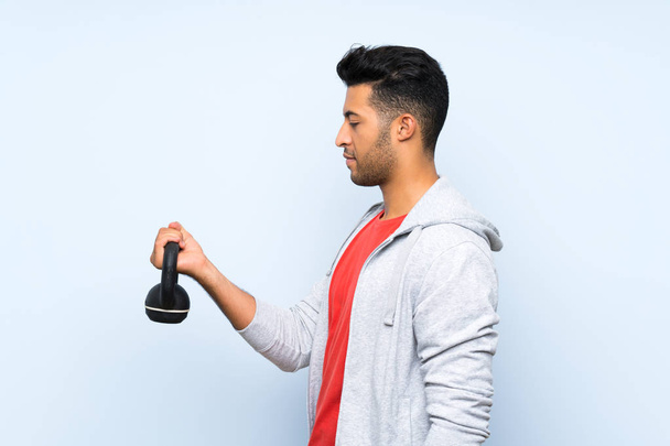 Sport man maken Gewichtheffen met Kettlebell over geïsoleerde blauwe muur - Foto, afbeelding