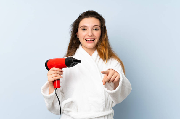 Young woman in a bathrobe with hair hairdryer points finger at you with a confident expression - Foto, Bild
