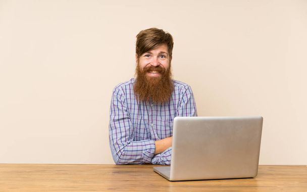 Vöröshajú férfi, hosszú szakálla egy asztalhoz, egy laptop nevetett - Fotó, kép