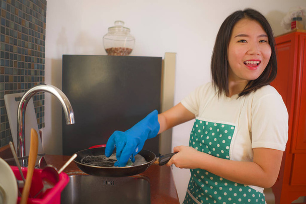 natural lifestyle portrait of young beautiful and happy Asian Korean woman in apron and rubber glove washing dishes and pan smiling cheerful in relaxed housework and domestic chores - Φωτογραφία, εικόνα