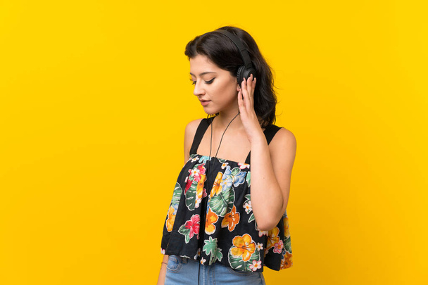 Mujer joven sobre fondo amarillo aislado escuchando música con auriculares
 - Foto, Imagen