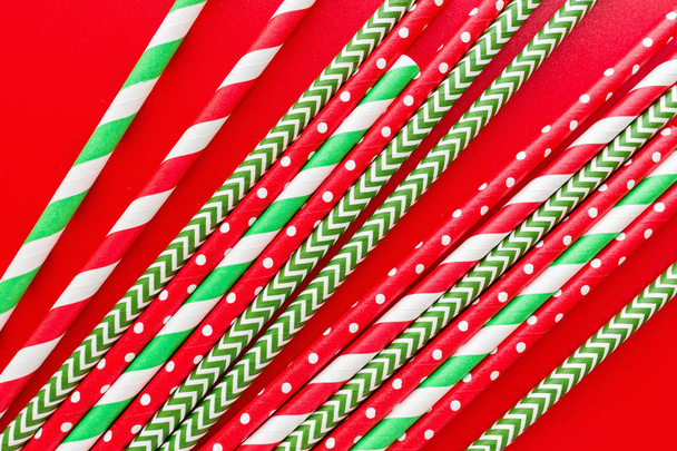 Striped drink straws of different colors on red background. New Year or Christmas pattern. Minimalism concept. Pop art style. Top view, Flat lay with straws used for drinking water or soft drinks. - Fotó, kép