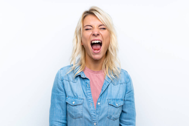 Молодая блондинка на изолированном белом фоне кричит в передней с широко раскрытым ртом
 - Фото, изображение