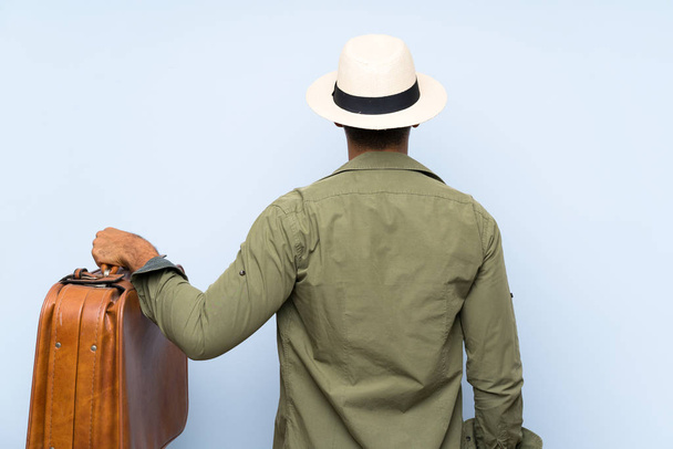 Молодой красивый мужчина держит винтажный портфель на изолированном синем фоне в задней позиции
 - Фото, изображение