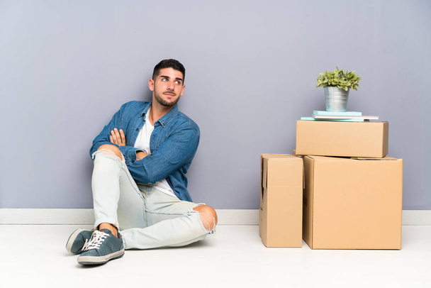 Красивый молодой человек переезжает в новый дом среди коробок, смеясь
 - Фото, изображение