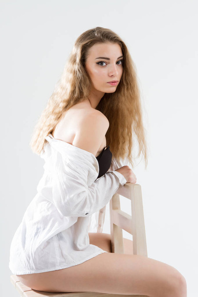 νεαρό κορίτσι που ποζάρει με λευκό ανδρικό πουκάμισο και μαύρα εσώρουχα. Πορτρέτο στούντιο. - Φωτογραφία, εικόνα