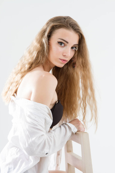 νεαρό κορίτσι που ποζάρει με λευκό ανδρικό πουκάμισο και μαύρα εσώρουχα. Πορτρέτο στούντιο. - Φωτογραφία, εικόνα