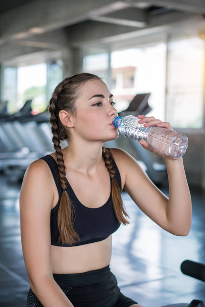 Piękna młoda kobieta pije wodę w siłowni. Sport odżywianie conc - Zdjęcie, obraz