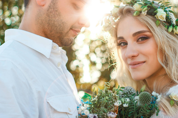 Bride in white dress and wreath and groom portrait in sunny summer day. Rustic outdoor wedding concept. Soft selective focus. - Foto, afbeelding