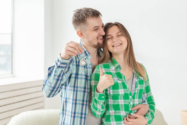 Młoda pozytywna para trzyma klucze do nowego mieszkania stojąc w ich salonie. Koncepcja ocieplenia i rodzinnego kredytu hipotecznego. - Zdjęcie, obraz