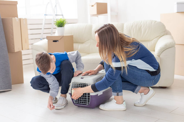 スリムな若い母親と小さな息子は、リビングルームで彼らの新しいアパートに彼らの美しい灰色のスコットランドフォールド猫を起動します。ハウスウォーミングと伝統の概念. - 写真・画像