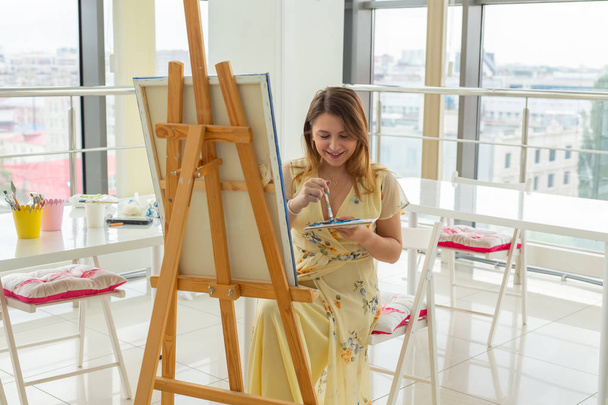Clase de arte, dibujo y creatividad - Estudiante sentada frente al caballete con paleta y pincel
 - Foto, Imagen